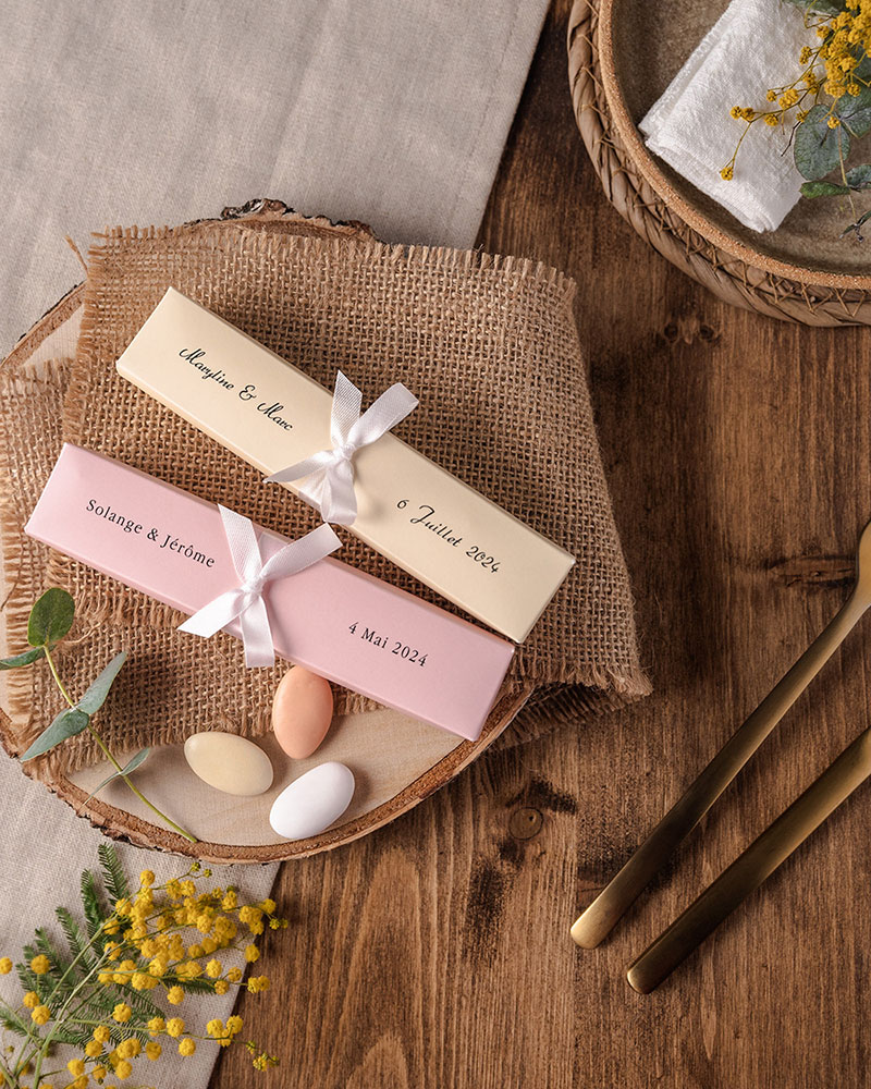 Dragées pour mariage dans des boîtes raffinées, disposées sur une assiette sur une table à la décoration rustique.