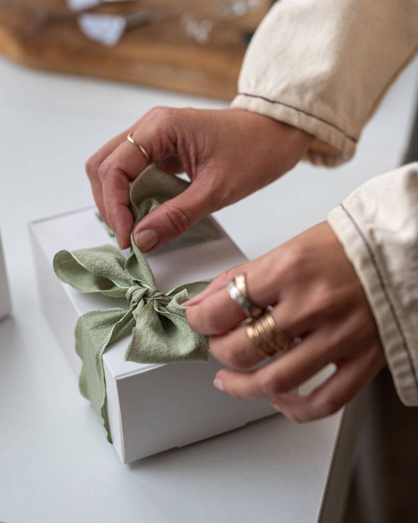 Mains délicates nouant un ruban satiné vert sur un cadeau, photographié pour l'identité visuelle d'une esthéticienne.