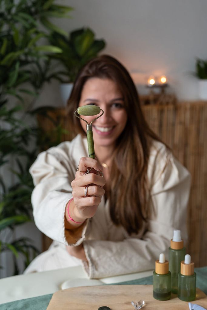 Une jeune femme souriante tendant un outil de massage facial vert à la caméra.