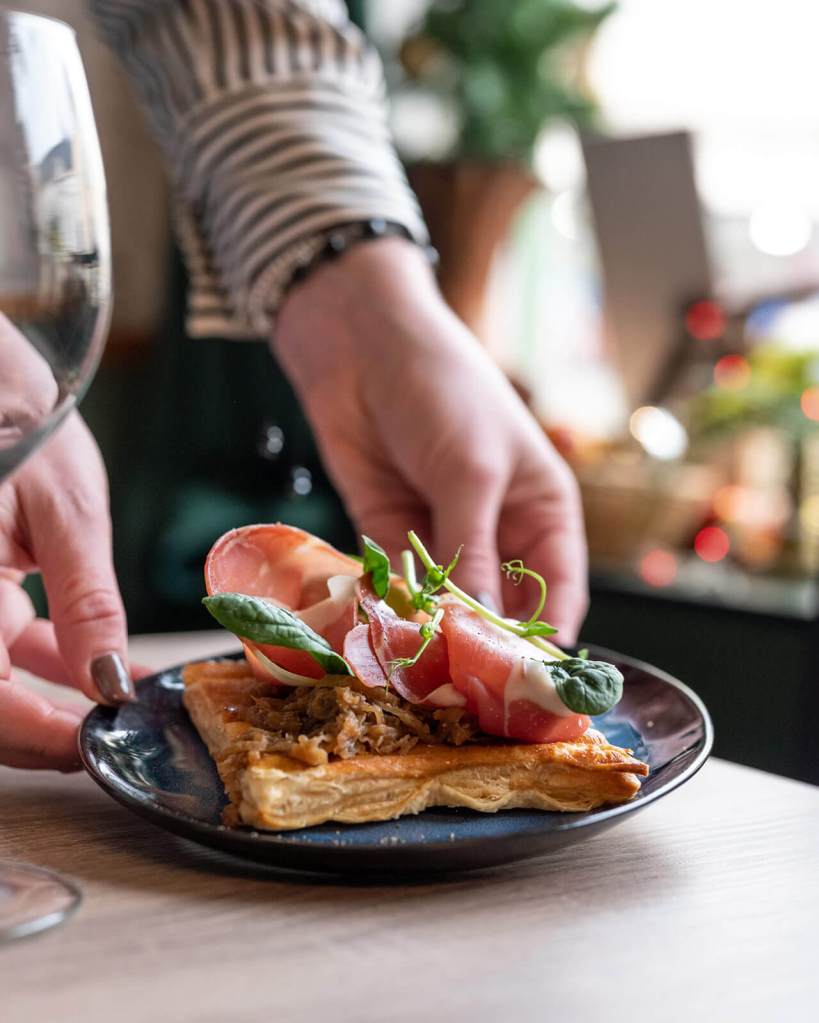 Photographie culinaire Paris, deux mains posent une assiette sur la table avec une gaufre salée, plat de restaurant élégant.