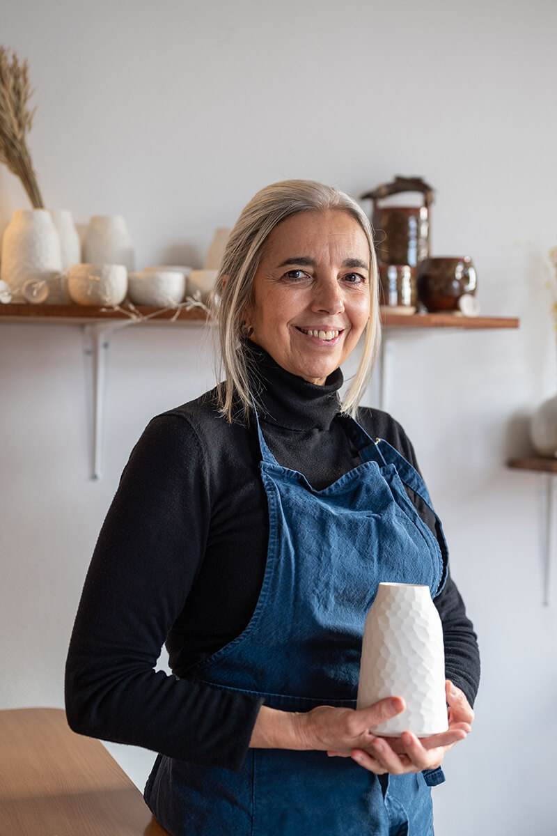Portrait souriant d'Ana, céramiste, tenant un vase qu'elle a créé dans son atelier à Paris.