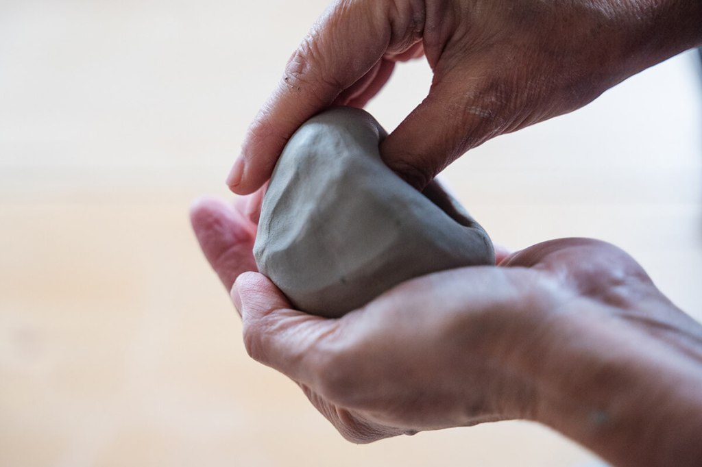 Gros plan sur les mains d'une céramiste modelant de l'argile avec précision et délicatesse.