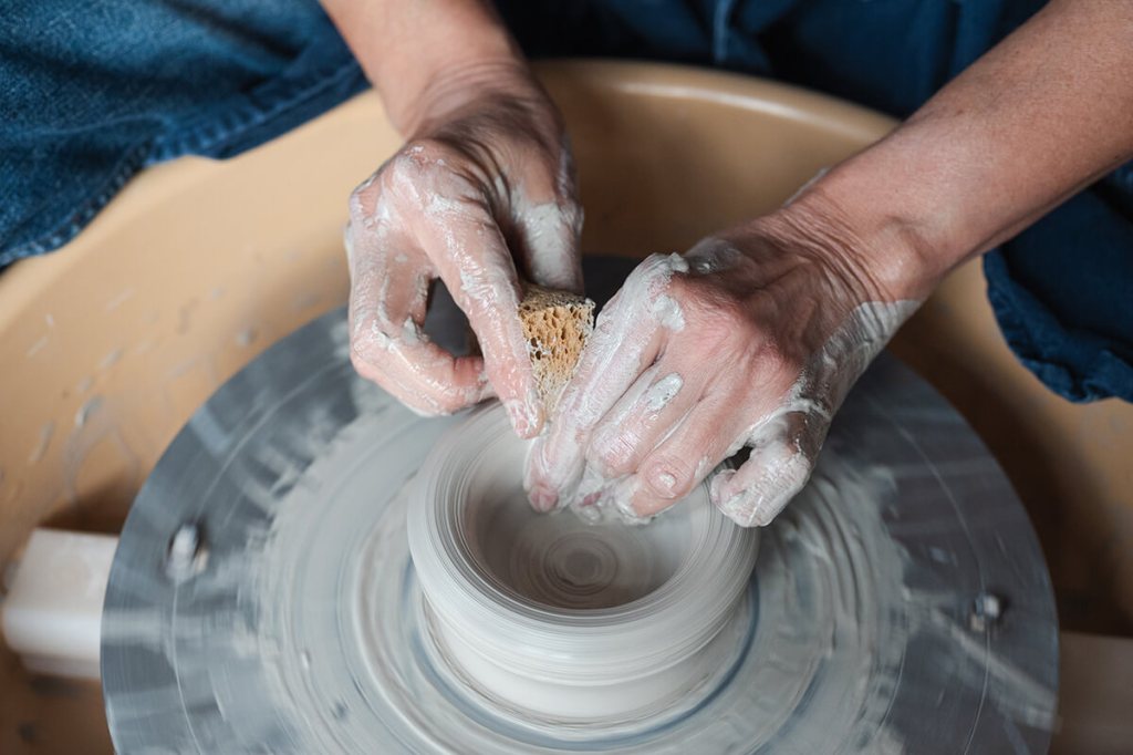 Mains d'une céramiste modelant une création en argile sur un tour de potier.