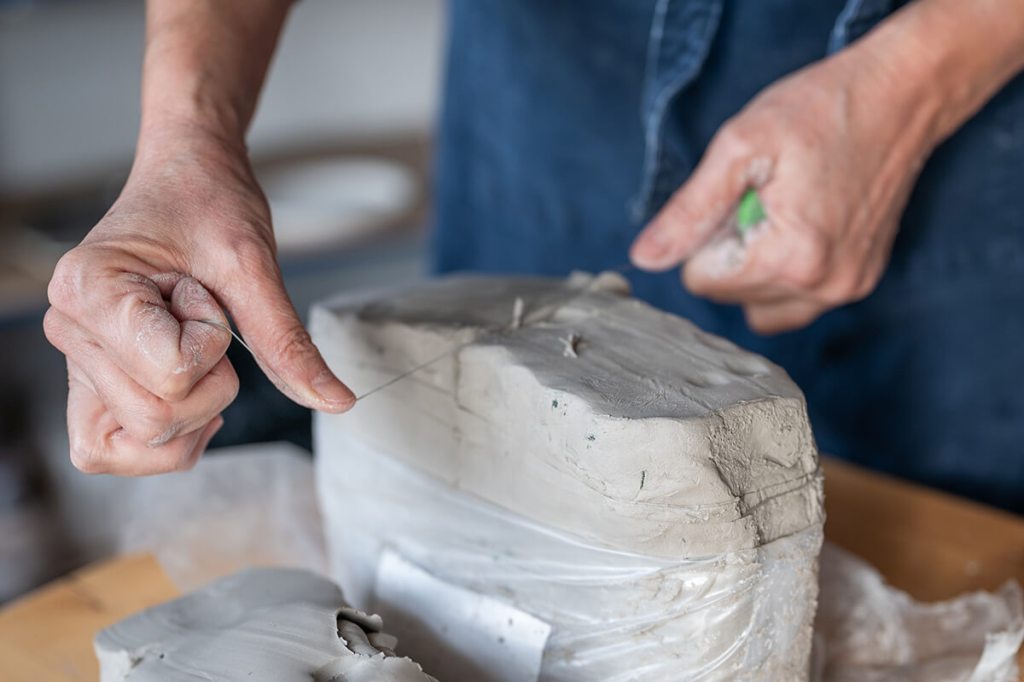 Mains d'une céramiste découpant un morceau d'argile à l'aide d'un fil en acier.