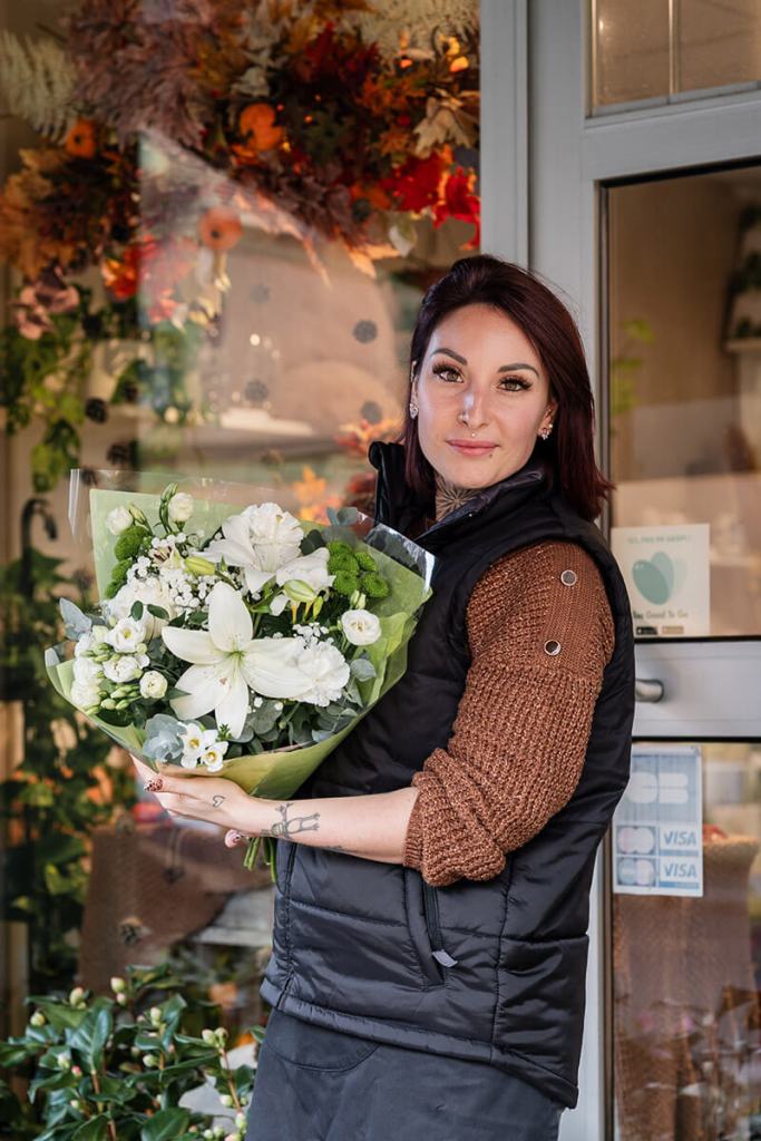 Portrait corporate de Mégane, fleuriste, tenant un bouquet de fleurs blanches devant sa boutique.